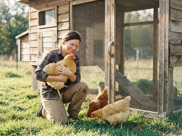 Homesteader with hens in front of cedar chicken coop